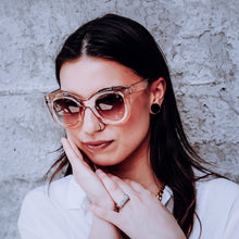 Load image into Gallery viewer, Woman wearing Teuila Fatupaito&#39;s Brown sunglasses &quot;Ms Jackson&quot; and a white top against a textured wall.
