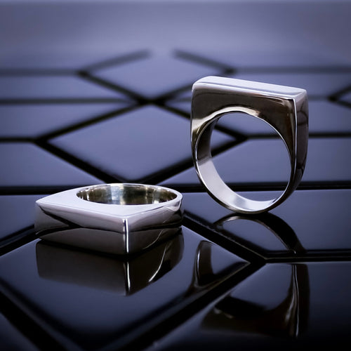 Two Teuila Fatupaito silver rings on a reflective black surface with geometric background