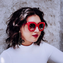 Load image into Gallery viewer, Woman wearing Teuila Fatupaito&#39;s Red sunglasses &quot;Ms Jackson&quot; and a white top against a textured wall.
